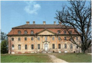 Schloss Meseberg, Ansicht im Frühjahr von der Parkseite im unrestaurierten Zustand. Die Fassade blättert ab, bauliche Mängel sind kaum zu übersehen. Rechts ragt ein alter Baum ins Bild.